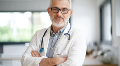 lekarz z siwą brodą w białym kitlu i stetoskopem na szyi